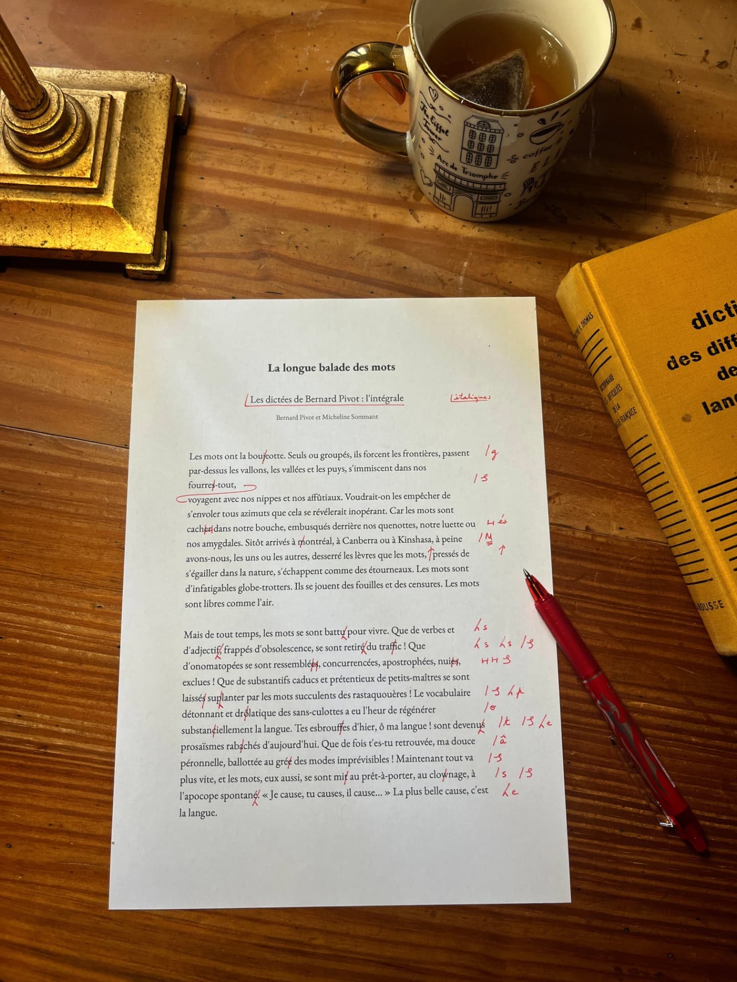 Le bureau d'Astrid : page annotée en rouge, dictionnaire des difficultés de la langue française, lampe en laiton et tasse de thé